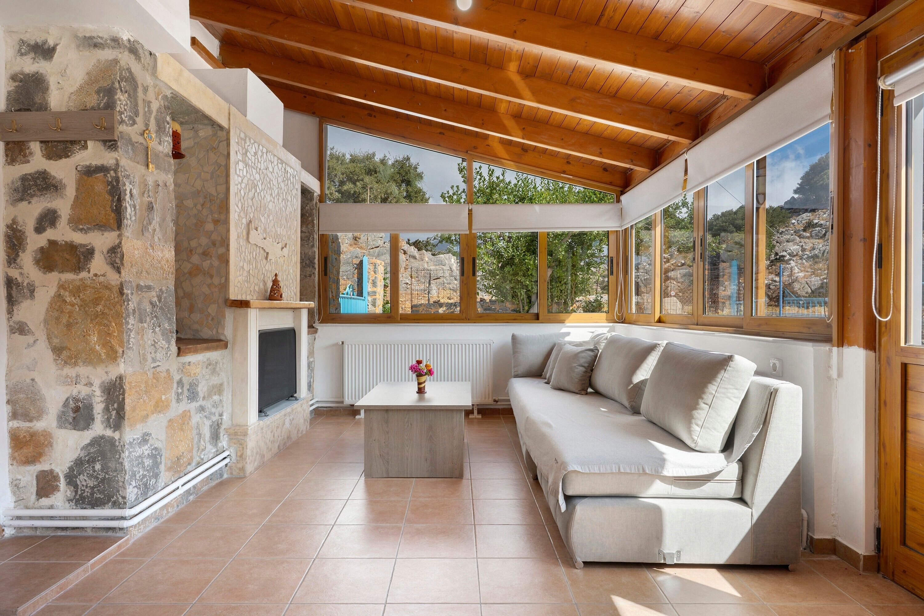 A cozy room with a stone wall, a wooden ceiling, a white sofa, and a view of the outdoors.