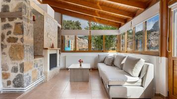 A cozy room with a stone wall, a wooden ceiling, a white sofa, and a view of the outdoors.