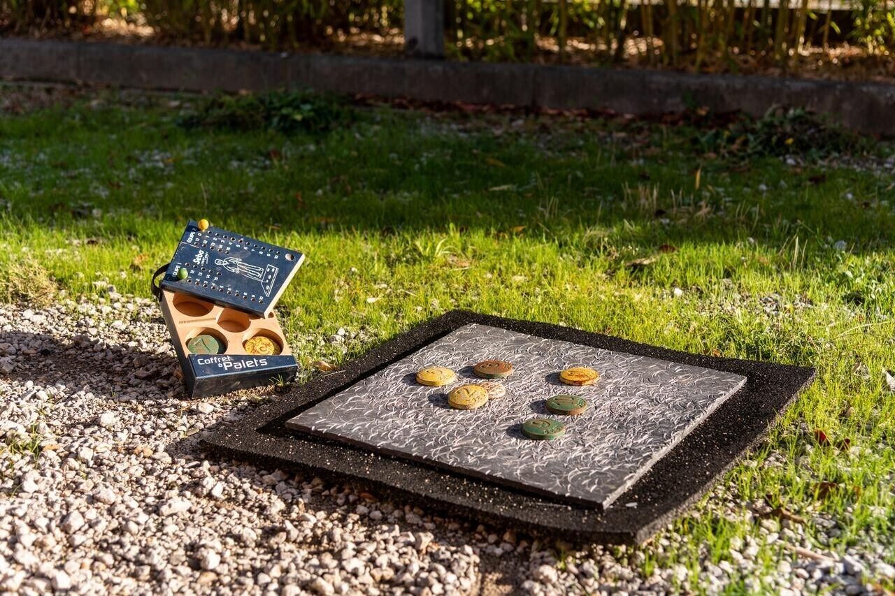 Ein tragbarer Grill mit einem Metallrost und einem Gestell, auf einem Kiesgrund mit Gras im Hintergrund.