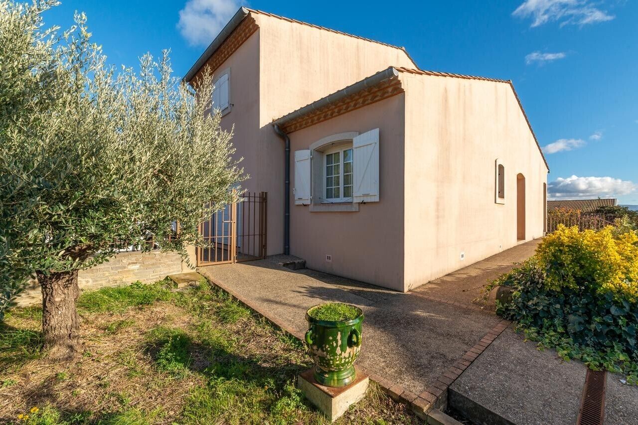 Un bâtiment d’un seul étage, doté d’un toit en pente, d’un petit porche et d’un espace jardin agrémenté d’un arbre et d’un bac à fleurs vert.