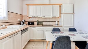 Una cocina con armarios blancos, lavavajillas, cafetera y una mesa con sillas.