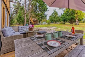 A patio with a wicker sofa, a wooden table set for dining, and a bottle of wine. - Domaine Les Maisons Des Houssats with Shared Pool (TRENSACQ)