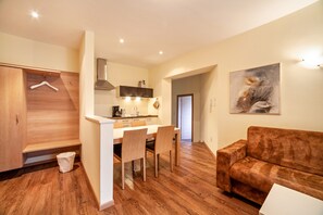 A modern kitchen with wooden cabinets, a dining area with chairs, a sofa, and a painting on the wall.