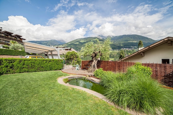 A residential area with a pond, greenery, and a mountain backdrop.