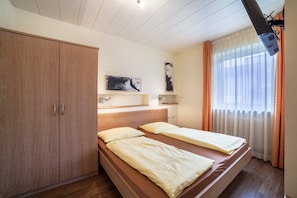 A room with a bed, wooden wardrobe, artwork on the wall, and a window with curtains.