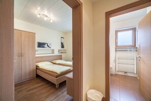 Une chambre avec une armoire en bois, un lit avec une tête de lit, une fenêtre et un radiateur.