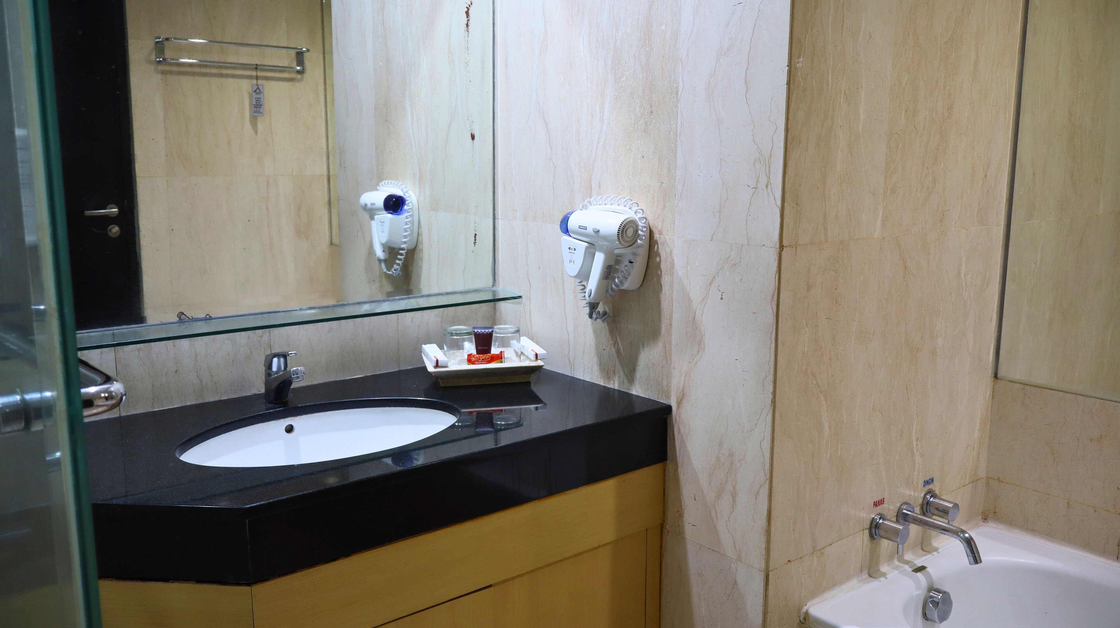 A bathroom with a black countertop, a white sink, a mirror, and two hair dryers mounted on the wall.