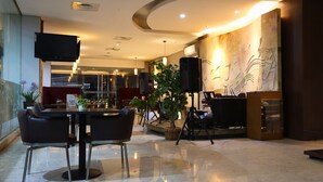 A modern hotel lobby with a reception desk, seating area, and a large abstract wall mural. - Amalia Hotel Lampung (Bandar Lampung)