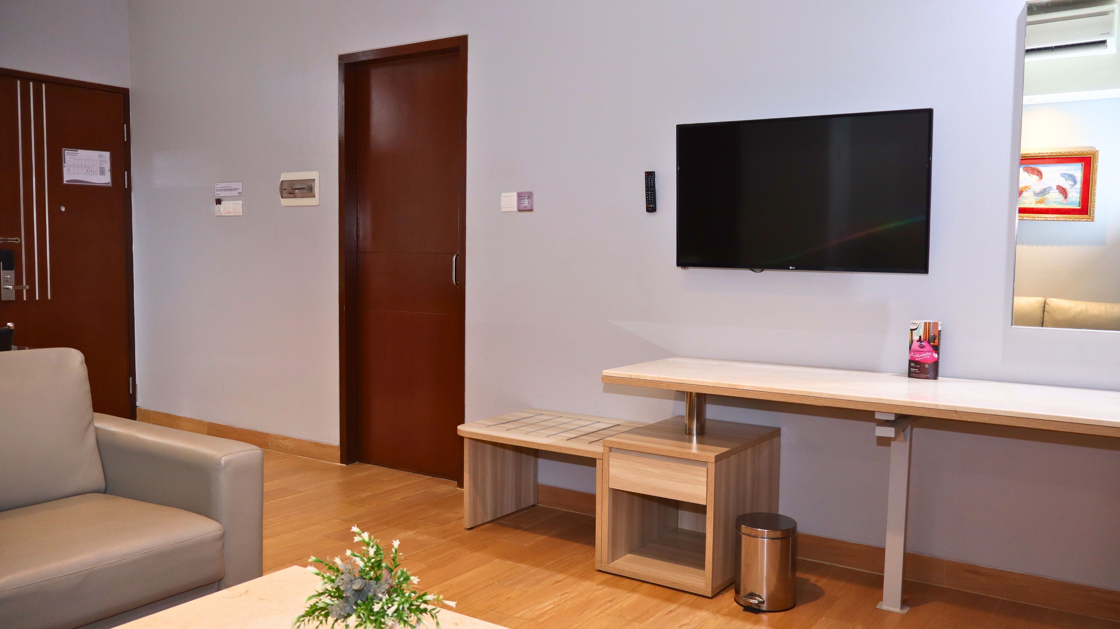 Una habitación de hotel moderna con un escritorio de madera, televisor, sofá y un cubo de basura.