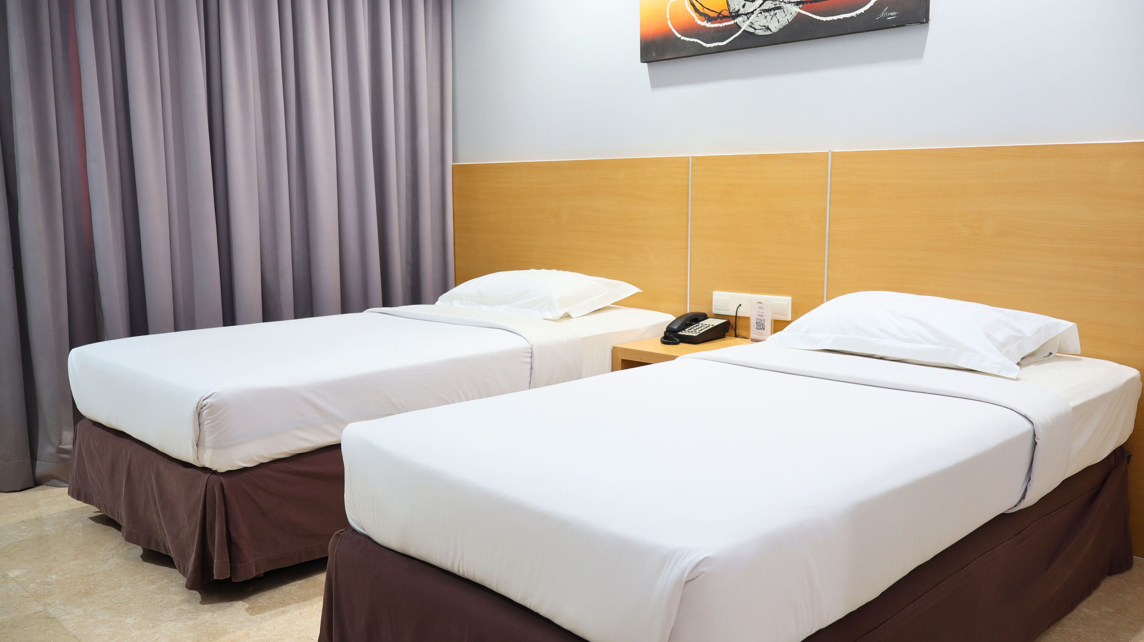 A hotel room with two single beds, a wooden headboard, a bedside telephone, and a painting on the wall.