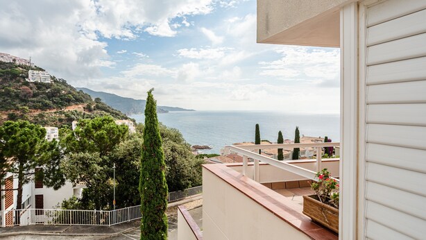 Ein Balkon mit Blick auf das Meer, ein weißes Gebäude und ein Baum.