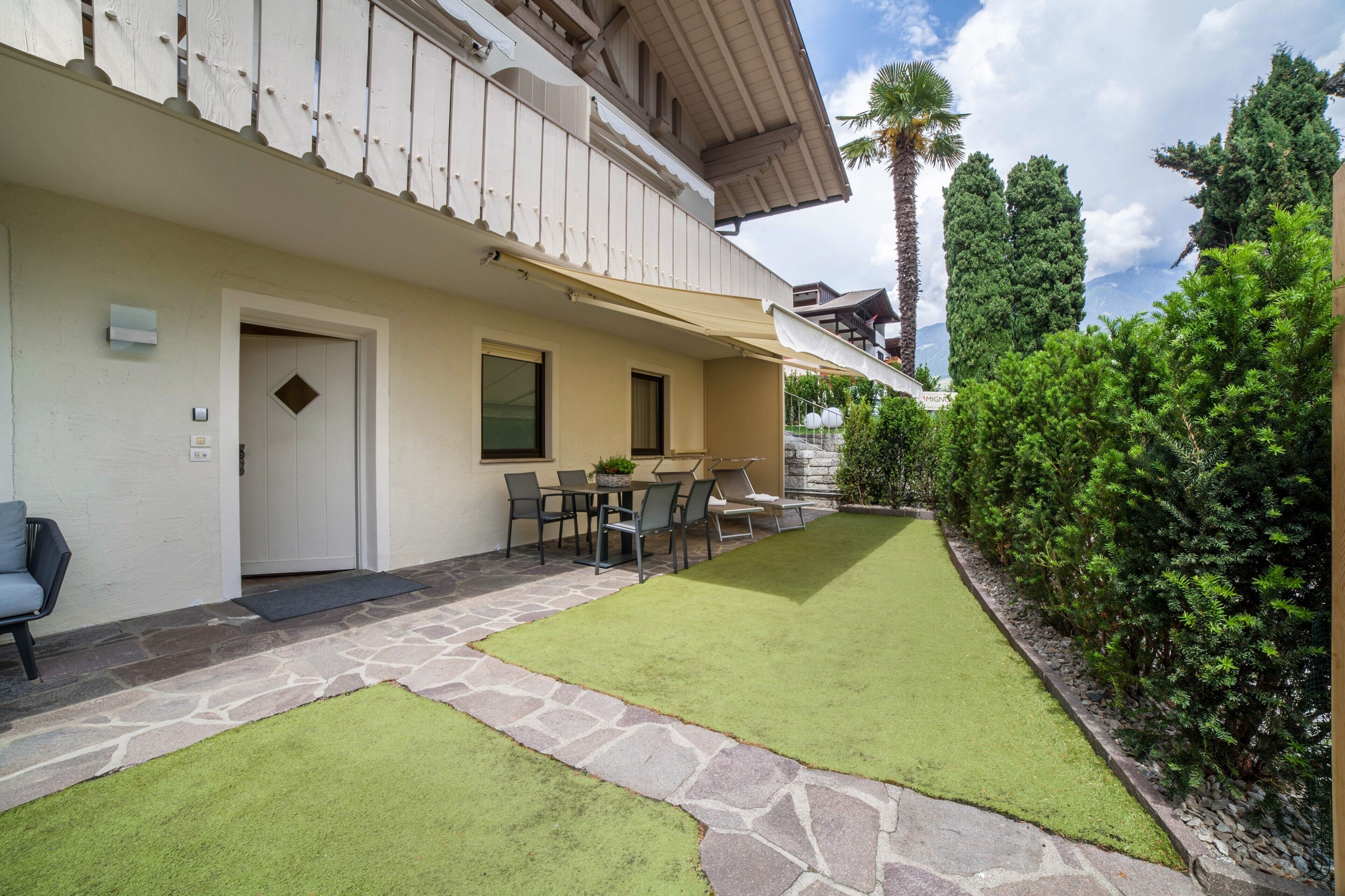 Un edificio con un patio in pietra, una zona pranzo con sedie e tavolo, e un prato curato.