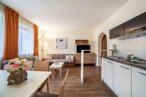 A modern living room with a sofa, coffee table, and a dining area. There is a kitchen with a sink and cabinets.