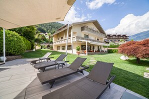 A hotel with a patio area featuring sun loungers, a covered seating area, and a mountain backdrop. - Holiday Apartment "Mignon 11" with Mountain View, Shared Heated Indoor Pool & Wi-Fi (Riffian)
