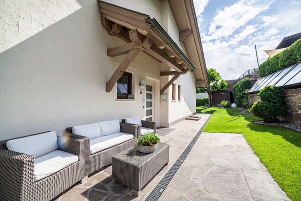 An outdoor patio with wicker furniture, a stone pathway, and a well-maintained lawn.