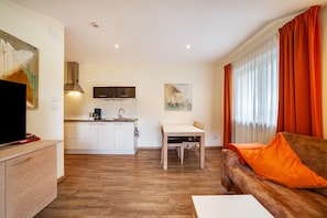 Una sala moderna con sofá, televisión, mesa de comedor y cocina con armarios y estufa.