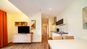 Habitación de hotel moderna con televisión de pantalla plana, suelo de madera, una mesa de comedor y una kitchenette.