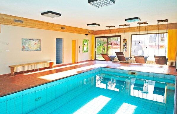 Una piscina con suelo de baldosas, un banco y una silla.