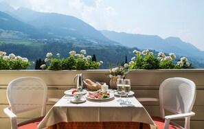 A table set with a meal, a pitcher, and glasses, overlooking a mountainous landscape.
