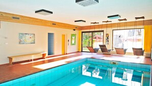 Una piscina con suelo de baldosas, un banco y una silla cerca de la orilla.