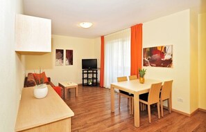 Un salon avec un téléviseur, un coin repas avec une table et des chaises, et un canapé avec des coussins.