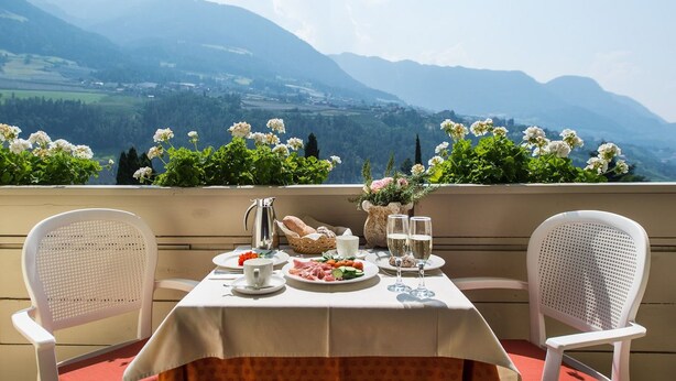 Una mesa para dos con vistas a las montañas, mantel blanco y una cesta de pan.