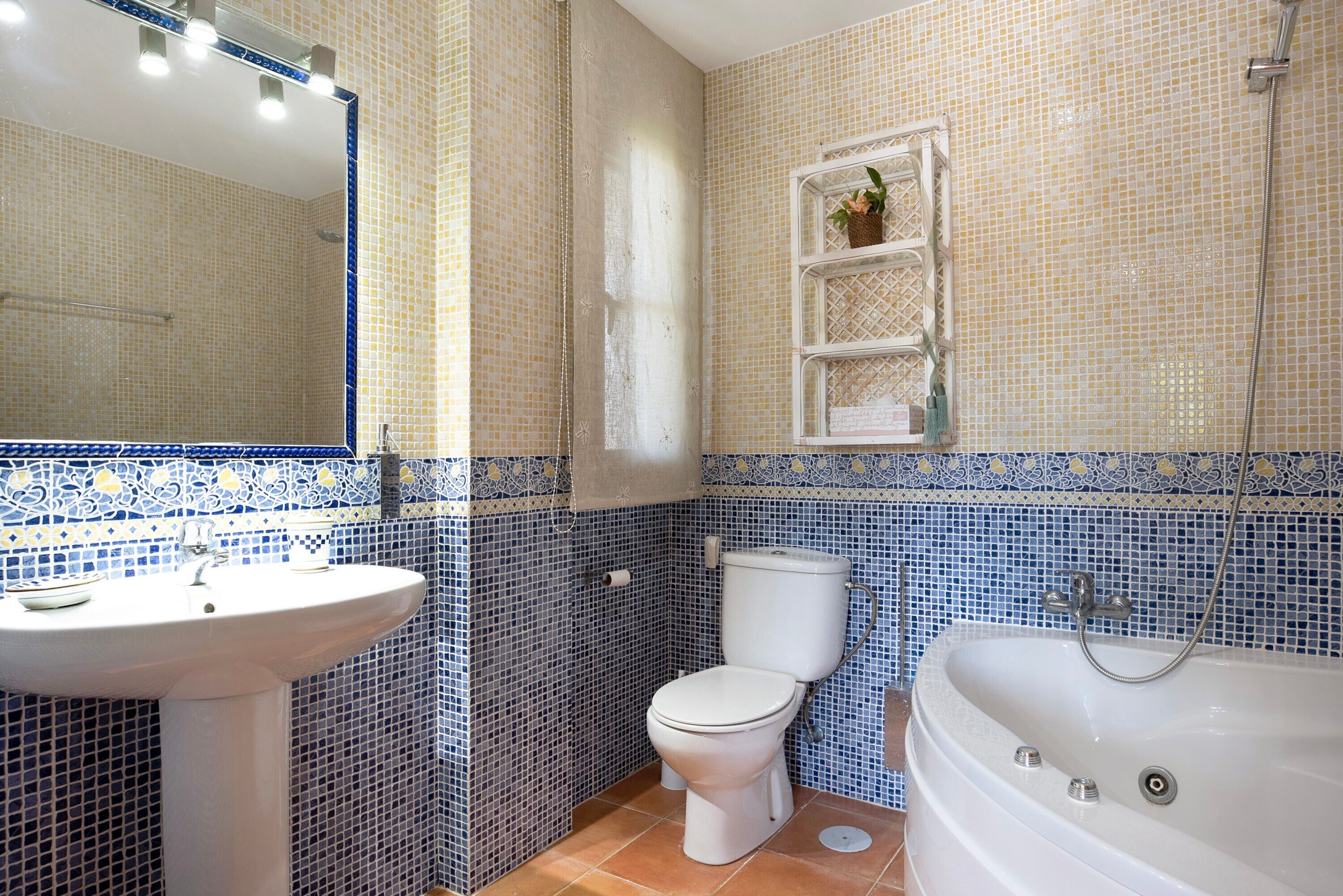 Een badkamer met een wastafel, toilet en bad, met blauwe en beige mozaïektegels.