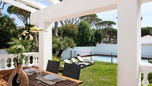 Une terrasse extérieure avec une table dressée pour le repas, une clôture blanche et une piscine en arrière-plan.