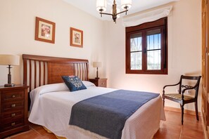 A bedroom with a wooden bed, two bedside tables with lamps, a chair, and a window with curtains.