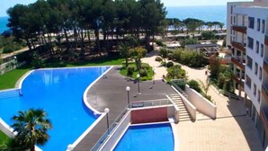 A swimming pool with a curved edge, a red diving platform, and a view of the sea.