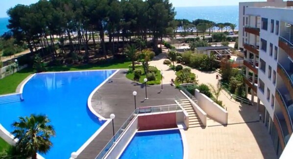 A swimming pool with a curved edge, a red diving platform, and a view of the sea.