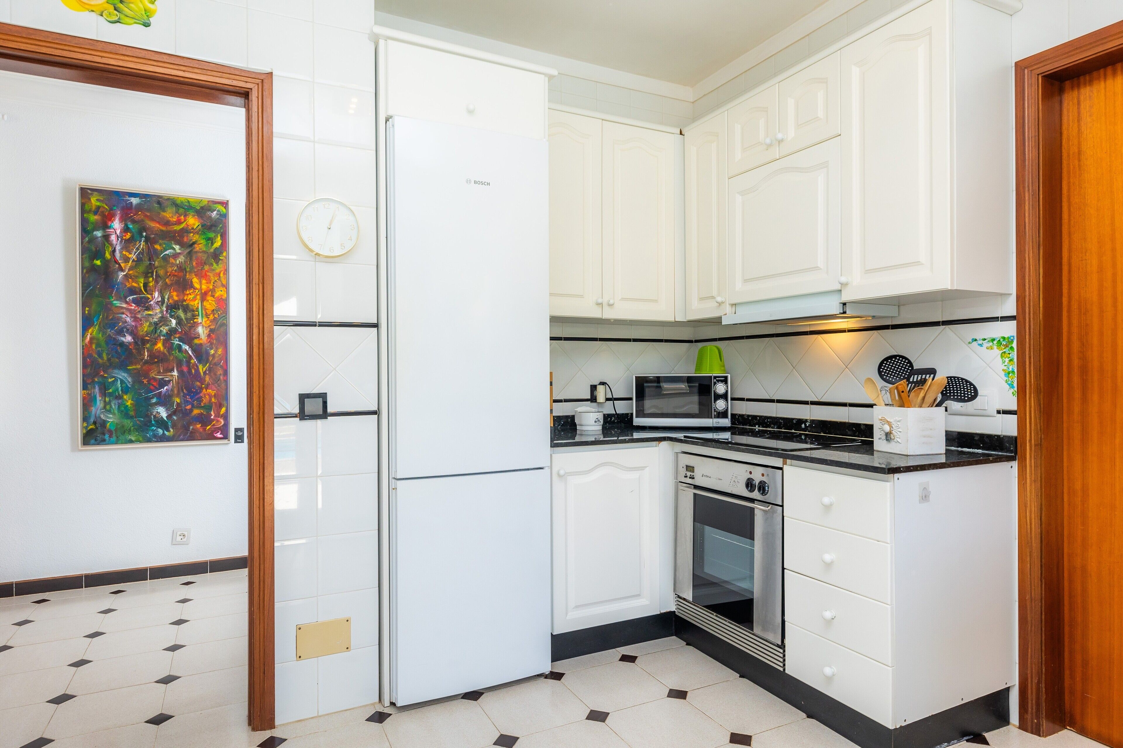 A kitchen with white cabinets, a Bosch refrigerator, a microwave, and an oven.