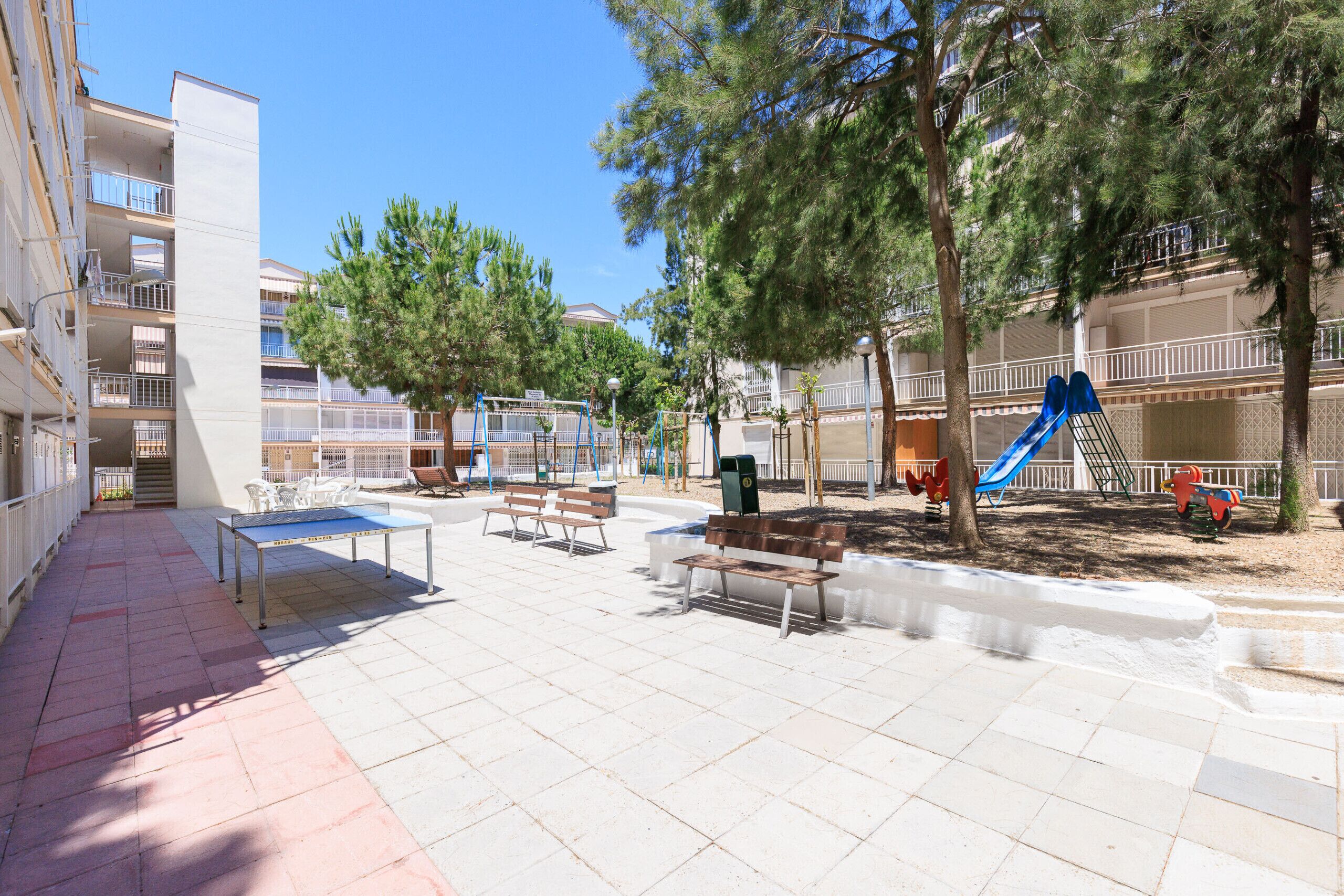 An outdoor area with a ping pong table, benches, and playground equipment including a slide.
