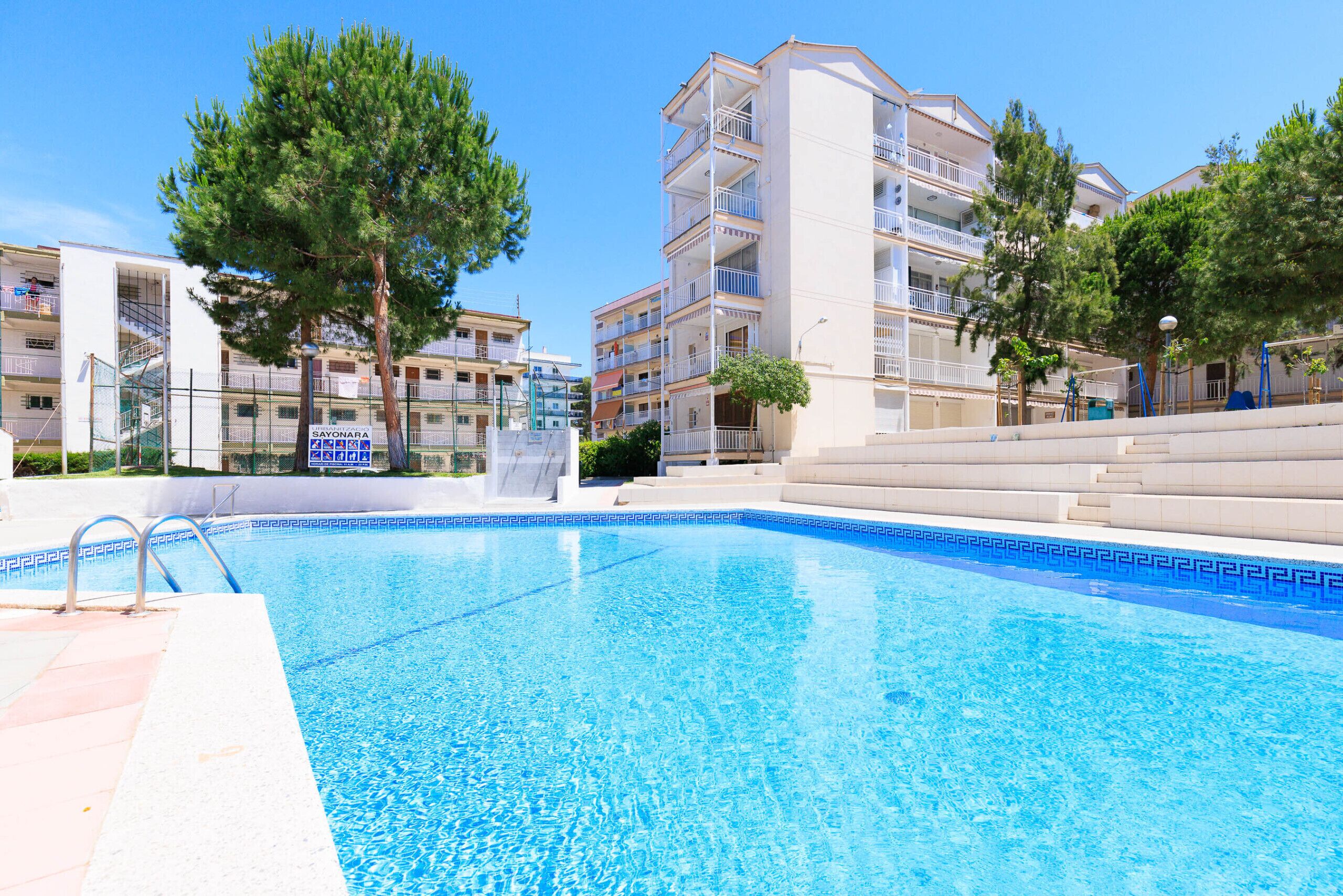 A swimming pool with a clear blue water, surrounded by apartment buildings and trees.