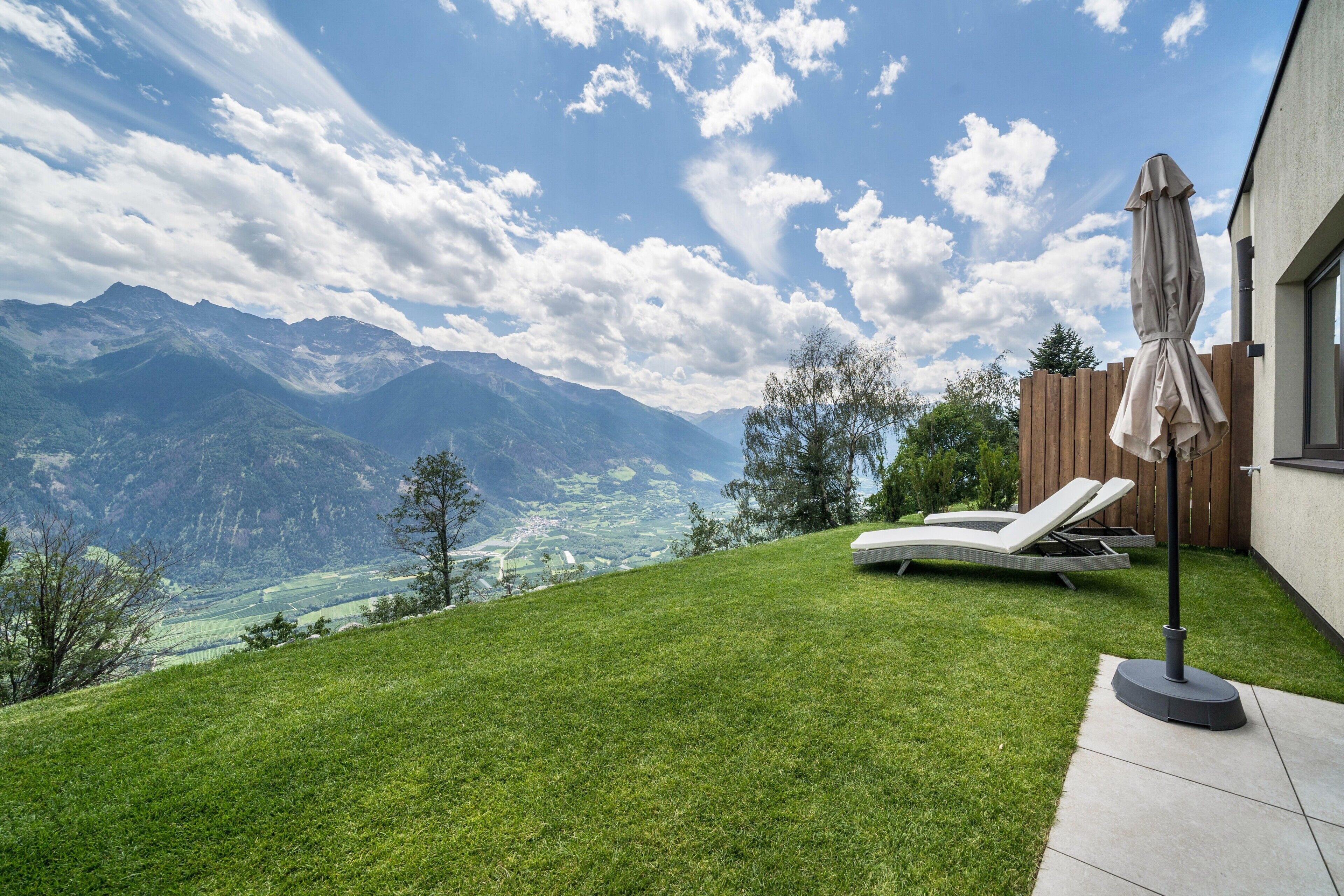 Un jardin avec une pelouse, une clôture en bois, un fauteuil de jardin et un parasol de patio.