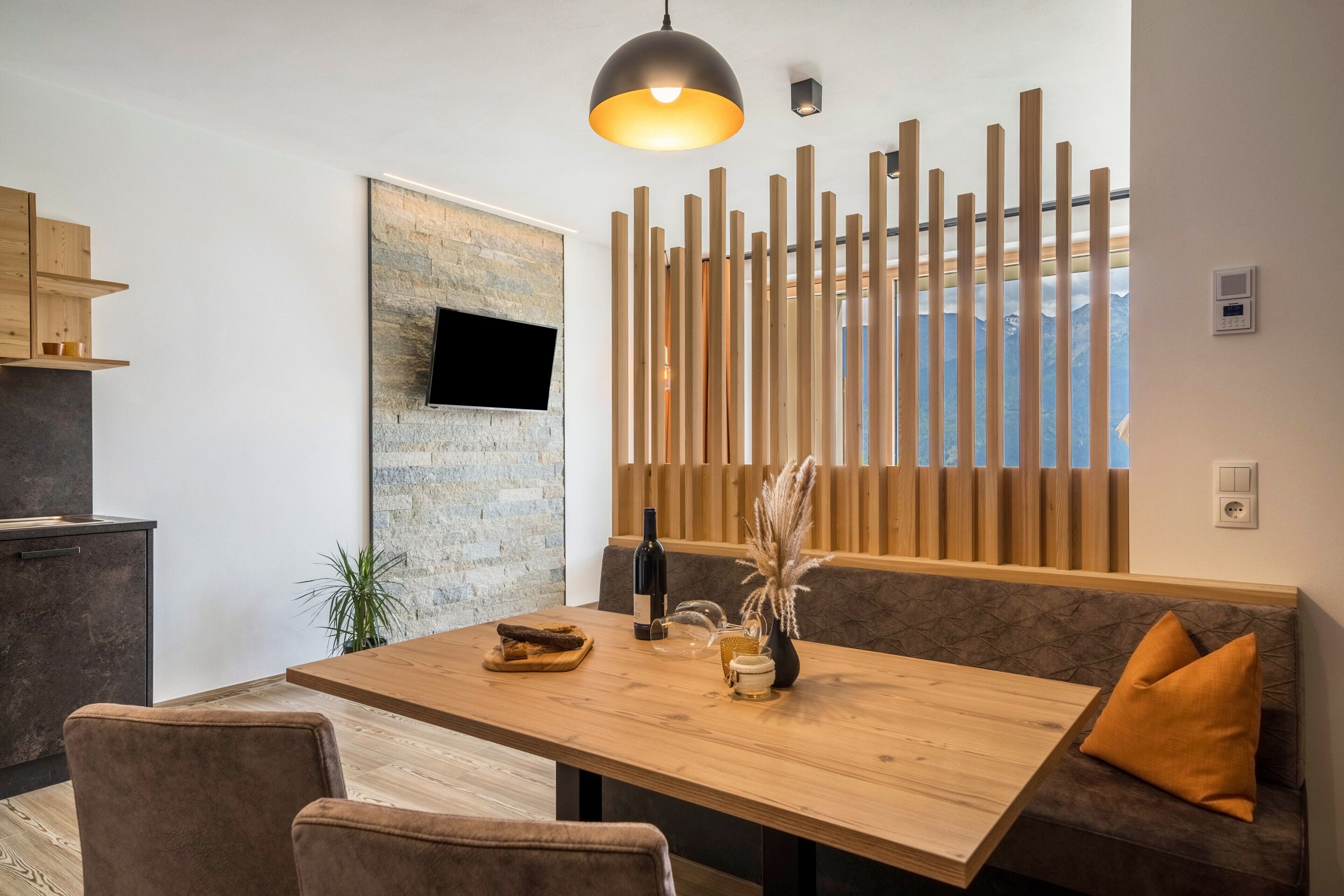 Een moderne eethoek met een houten tafel, beklede zitplaatsen, een wandgemonteerde televisie en een decoratief houten paneel.