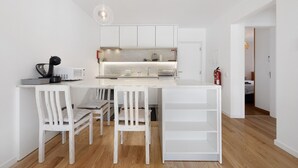 Une cuisine compacte avec des meubles blancs, un îlot central et un coin repas avec des chaises blanches.