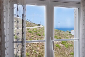 A coastal view through a window with a metal railing and a pathway leading to the sea.