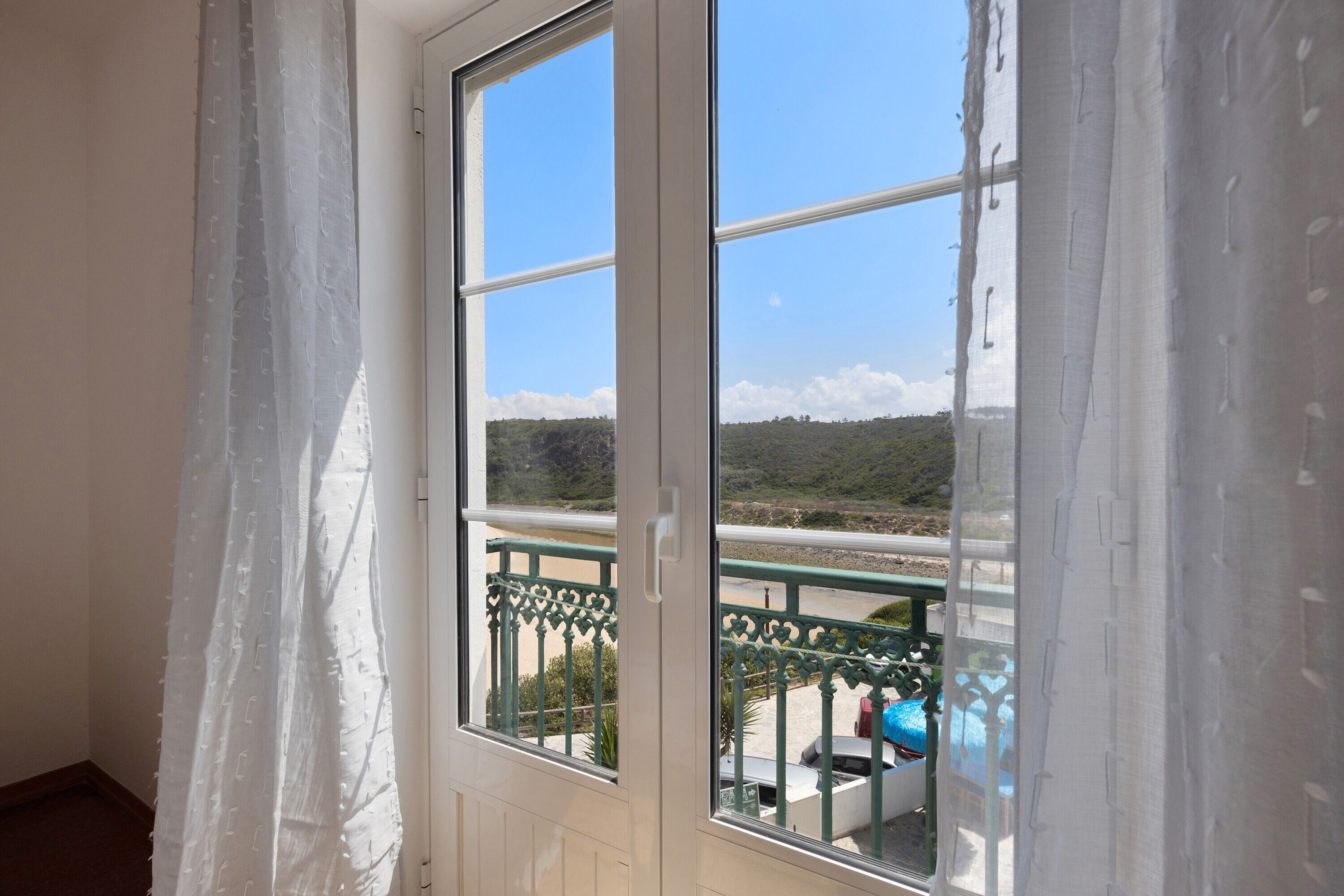 Ein Balkon mit Blick auf eine Küstenlandschaft, einem Geländer und einer Tür mit Vorhängen.