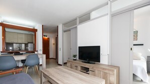 A modern hotel room with a wooden dining table, a TV, and a bed. - UHC NOVELTY APARTMENTS 144 (Salou)