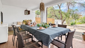 Un espace de restauration en plein air avec une table dressée pour quatre personnes, des chaises en osier et un luminaire suspendu.