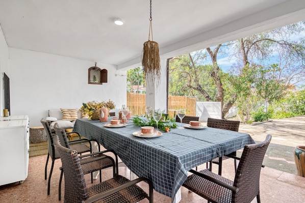 An outdoor dining area with a table set for four, wicker chairs, and a hanging light fixture.