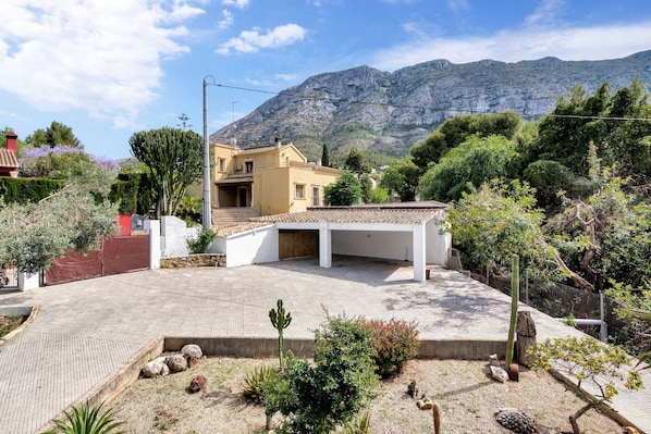 Un quartiere residenziale con una casa, un vialetto asfaltato e una montagna sullo sfondo.