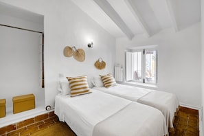 A bedroom with two beds, a window with a view, and a brick wall.