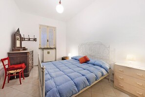 Ein Schlafzimmer mit Bett, Schminktisch, Stuhl, Spiegel und einem Fenster mit Vorhängen.