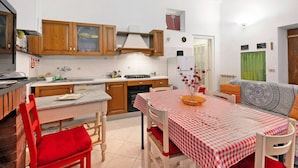 A compact kitchen with wooden cabinets, a dining table with a checkered tablecloth, and a red chair. - Holiday Apartment "Giomar" (levanto)