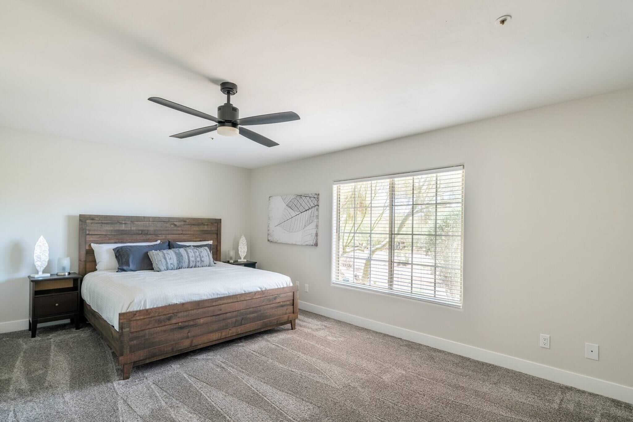 Une chambre à coucher avec un lit, un ventilateur de plafond, une fenêtre avec des stores et une table de chevet.