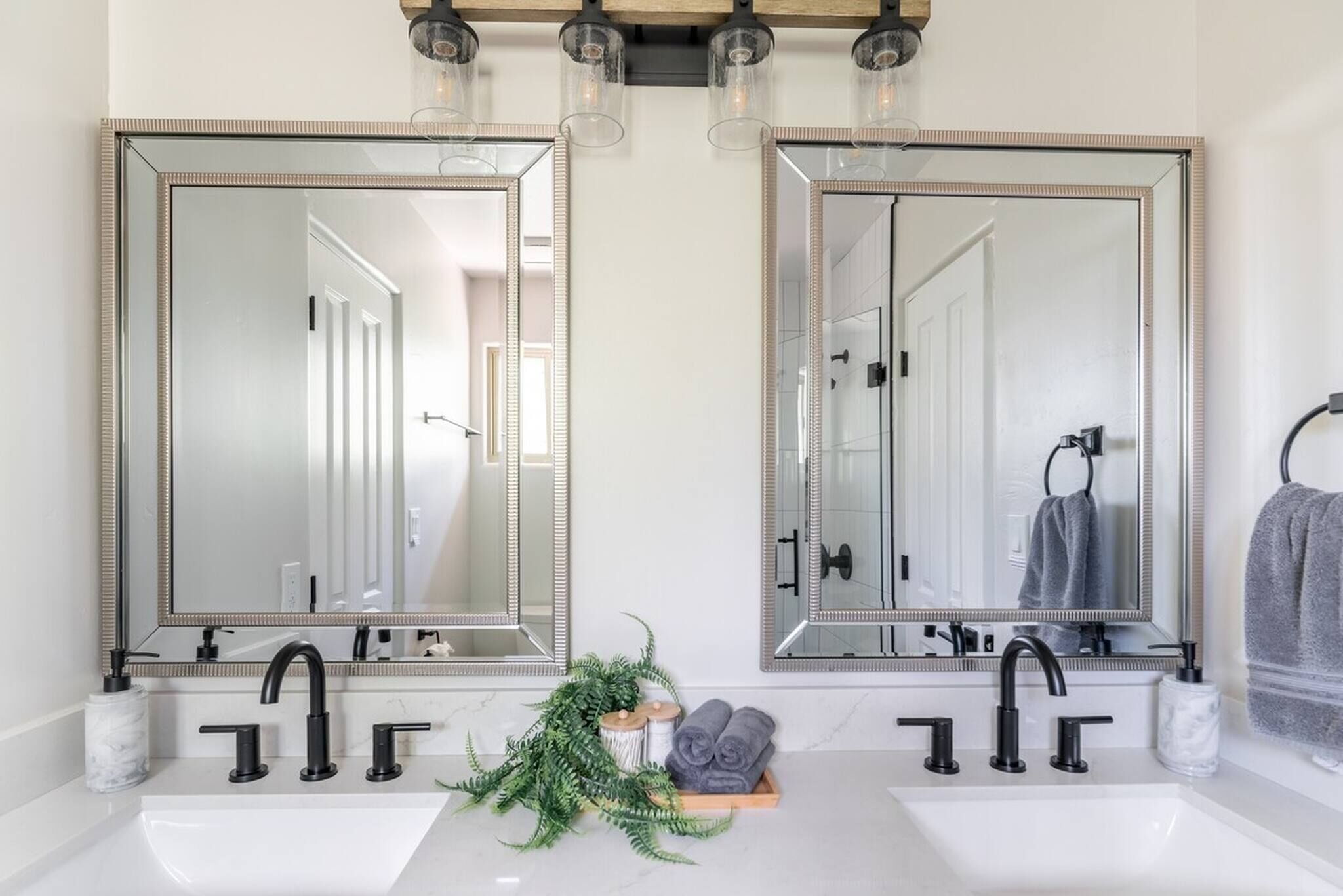 A bathroom with two large mirrors, a white sink, black faucets, and a small plant on the counter.