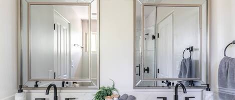 A bathroom with two large mirrors, a white sink, black faucets, and a small plant on the counter.