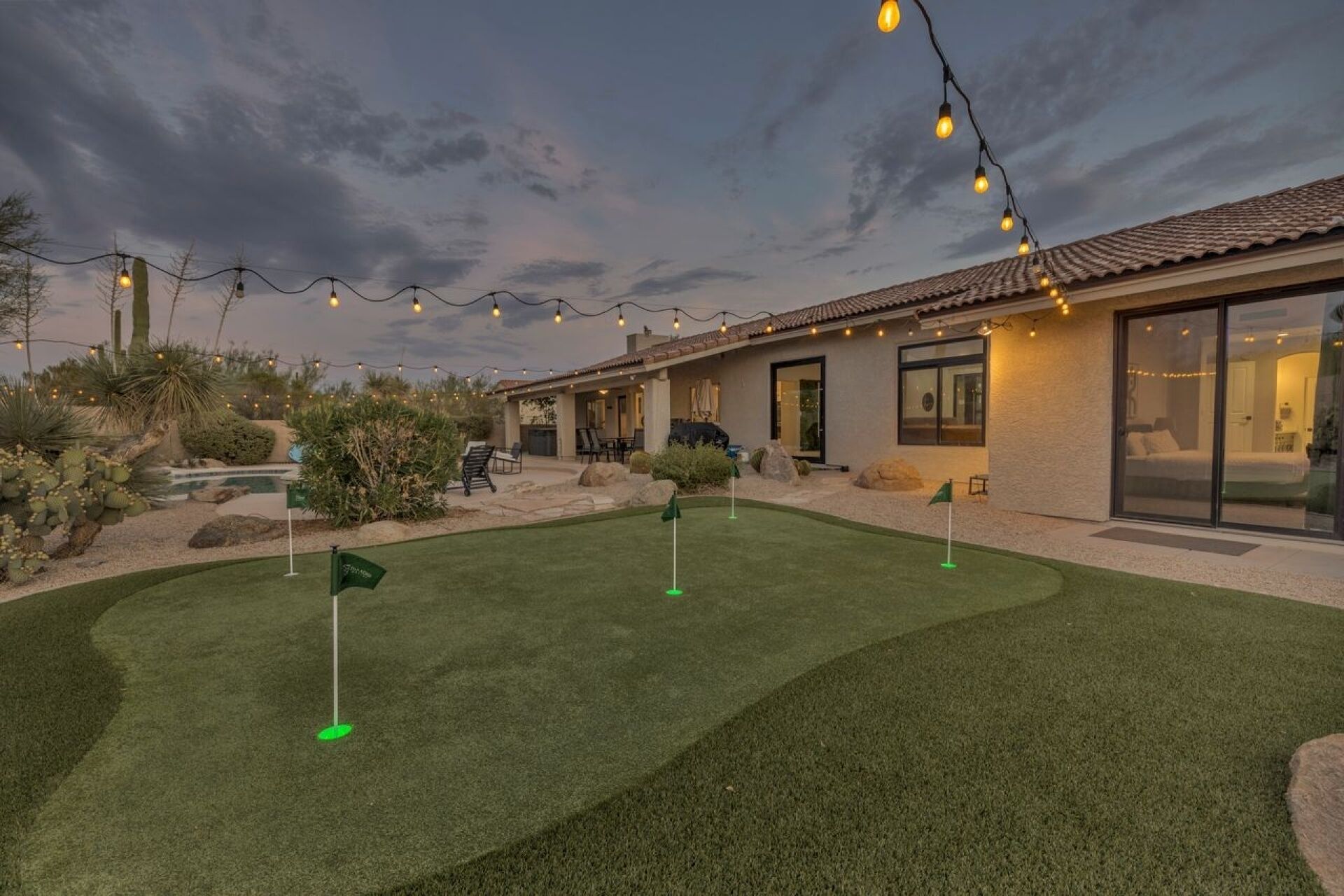 Il s’agit d’une propriété résidentielle dotée d’un jardin avec une pelouse artificielle, d’une terrasse aménagée avec du mobilier d’extérieur et de guirlandes lumineuses.